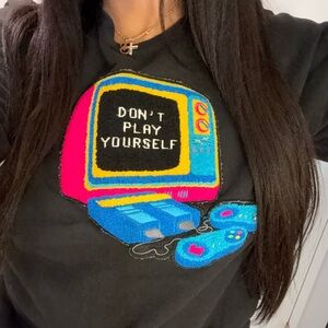 Black crewneck graphic pullover with tufted decal “don’t play yourself”